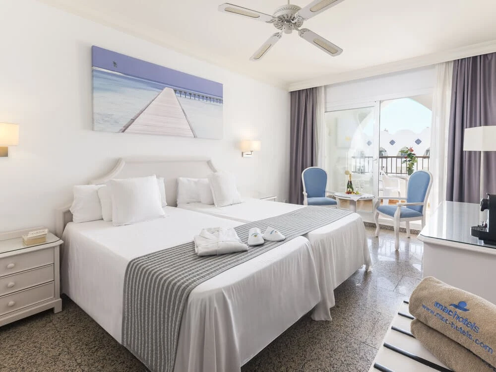 Dormitorio luminoso con cama blanca, sillones azules y balc&oacute;n exterior