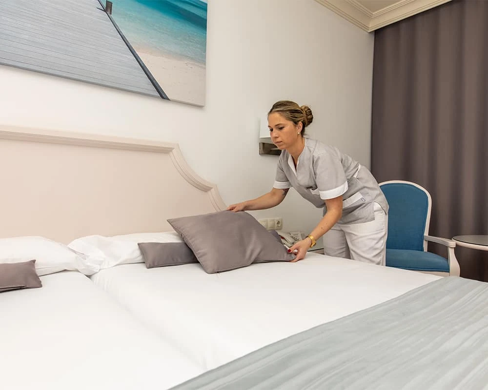 Enfermera ajusta una almohada y colcha en una cama de habitaci&oacute;n hospitalaria.