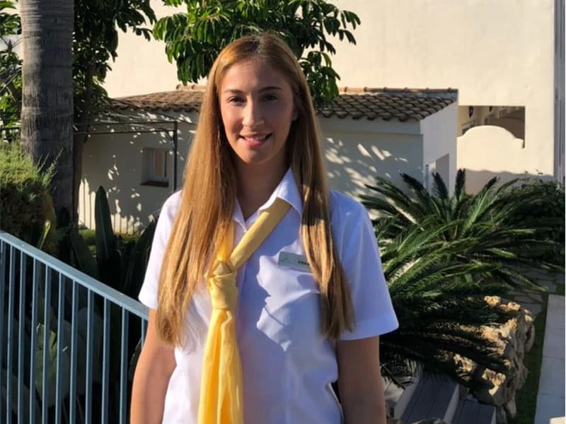 Joven con uniforme escolar amarillo y blanco, sonriendo en jard&iacute;n.