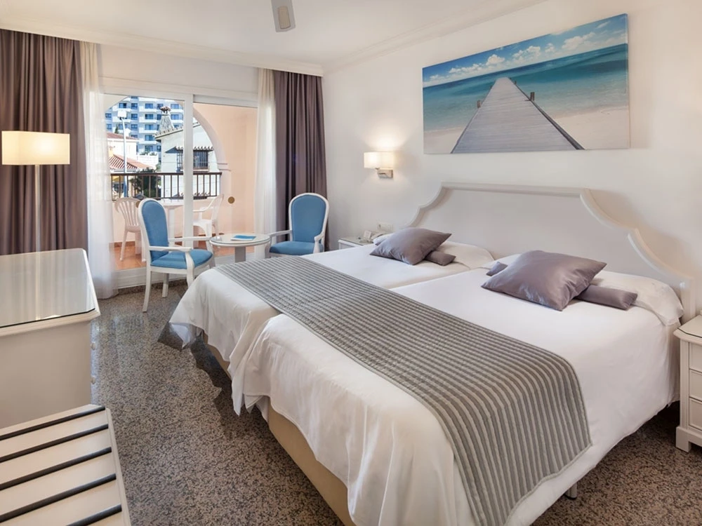 Dormitorio moderno con cama doble, ventana y balc&oacute;n, vista al mar.
