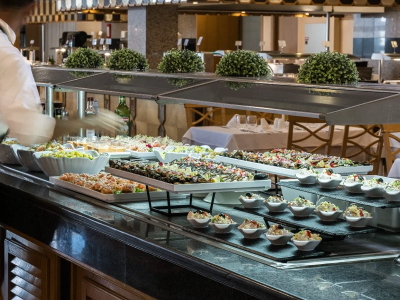 Buffet con bandejas y platos de comida y ensaladas en mesa de hotel