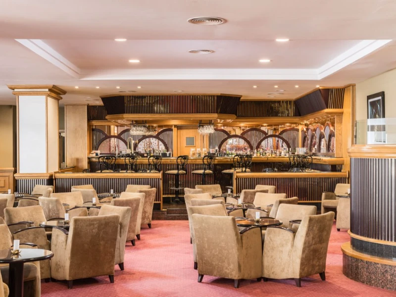 Sala de bar con asientos, barra dorada y luces, estilo cl&aacute;sico.