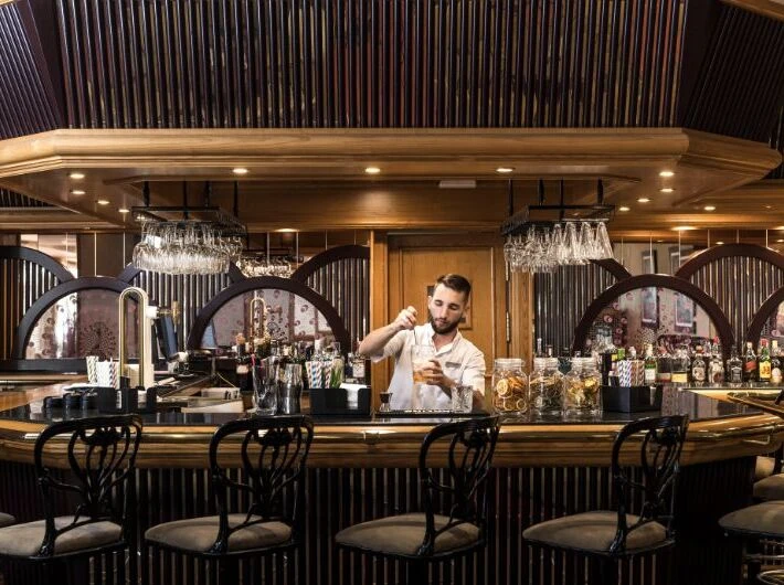 Bartender prepara c&oacute;ctel en barra con l&aacute;mparas de cristal y bebidas.