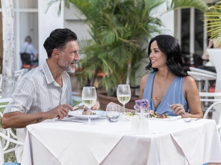 Pareja conversando en una mesa con copas de vino en una terraza al aire libre.