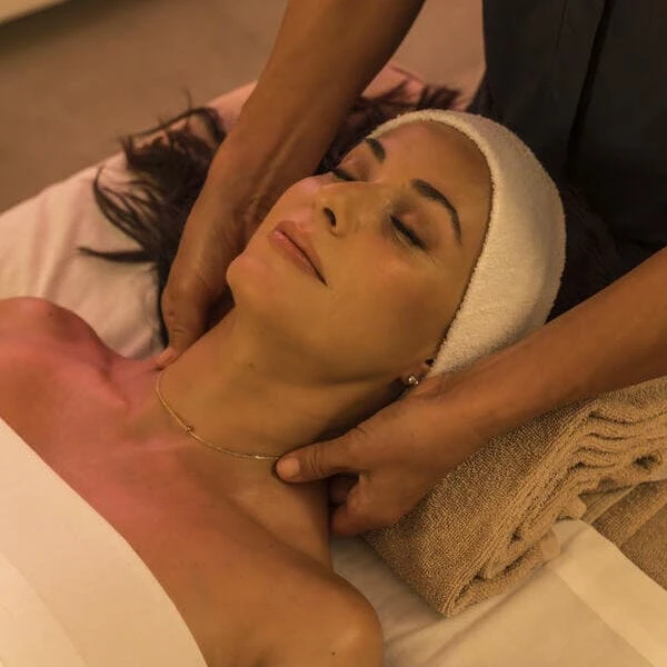 Mujer con toalla sobre el rostro, masaje con manos y aceites en spa