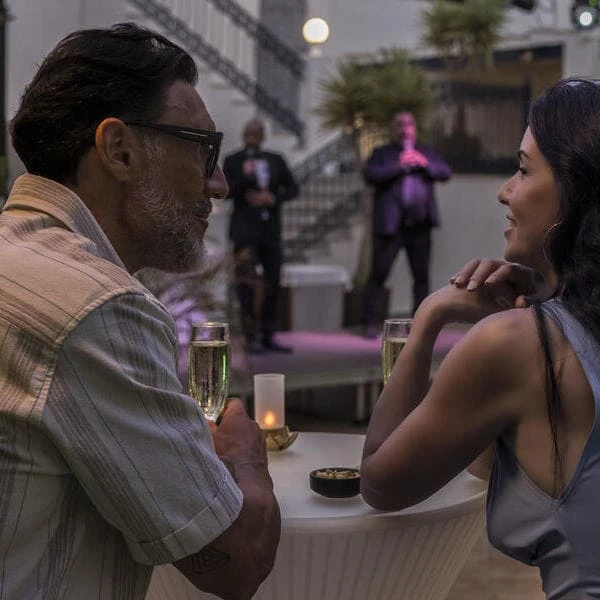 Dos personas conversan en una cena al aire libre con m&uacute;sica al fondo.