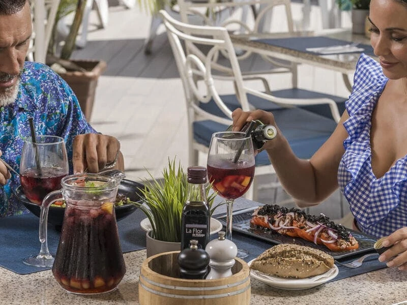 Pareja en terraza sirve vino y prepara una comida con parrilla y ensalada