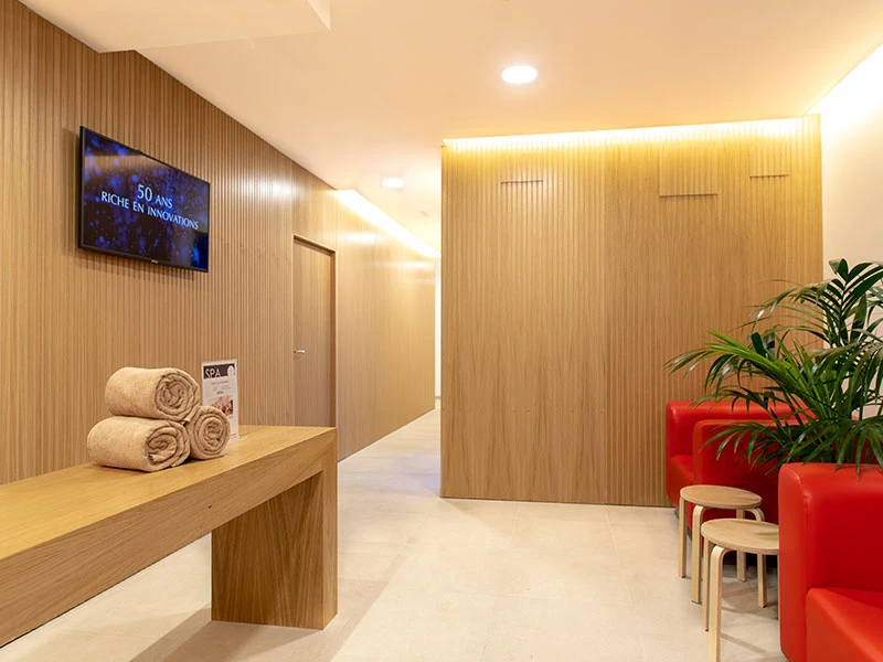 Recepci&oacute;n tipo spa con madera, sillas y planta decorativa, pasillo iluminado