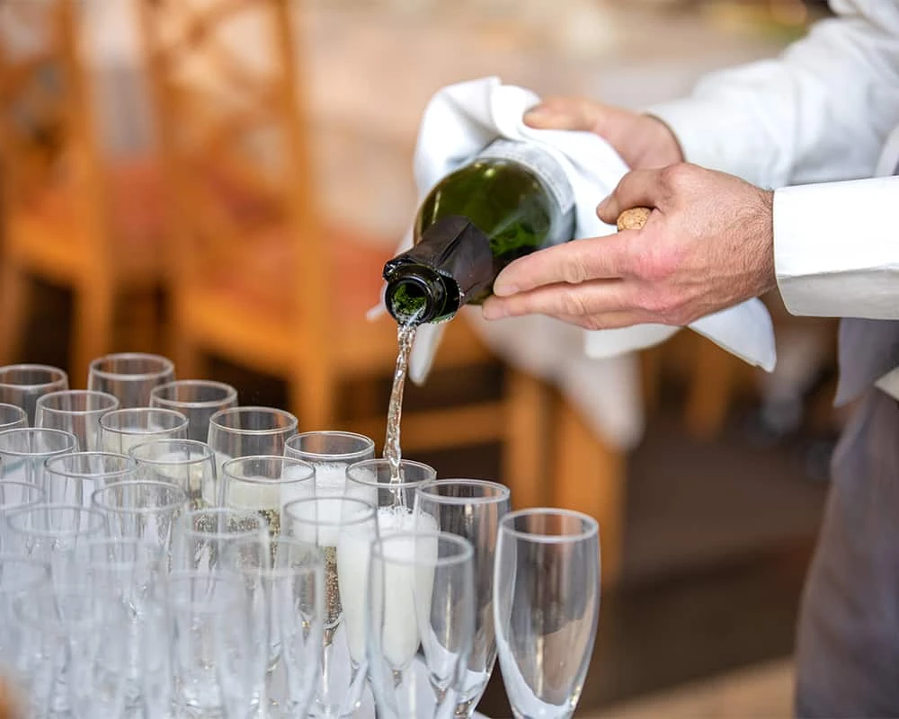 Sirviendo champ&aacute;n desde una botella verde en copas de cristal en evento