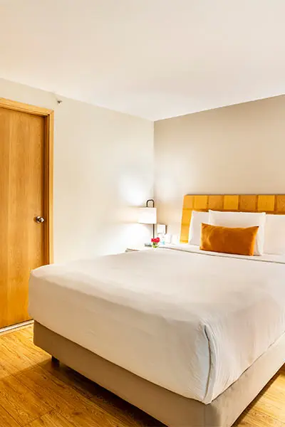 Habitaci&oacute;n de hotel con cama doble blanca y ventana de madera