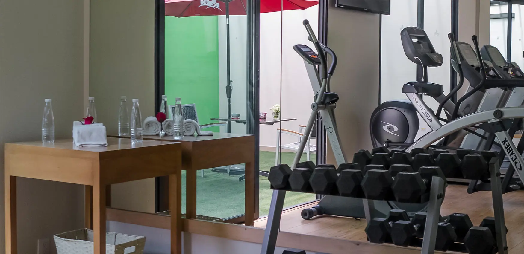 Gimnasio con mancuernas y bicicleta elíptica junto a mesa de oficina.