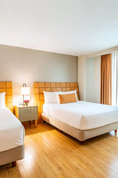 Habitaci&oacute;n de hotel con dos camas y ventanas con cortinas de color miel