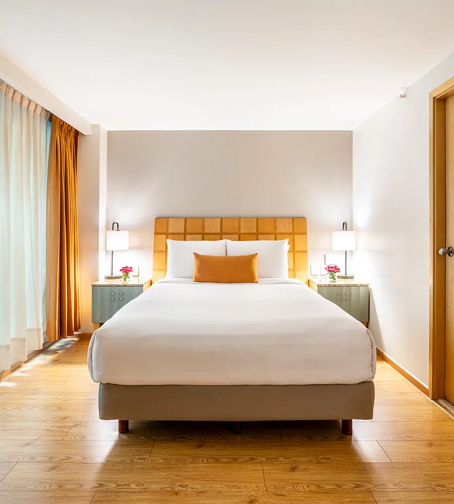 Dormitorio moderno con cama doble, mesitas y l&aacute;mparas de pared.