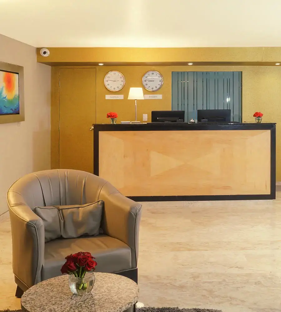 Recepci&oacute;n de hotel con mostrador, relojes y sillas grises.