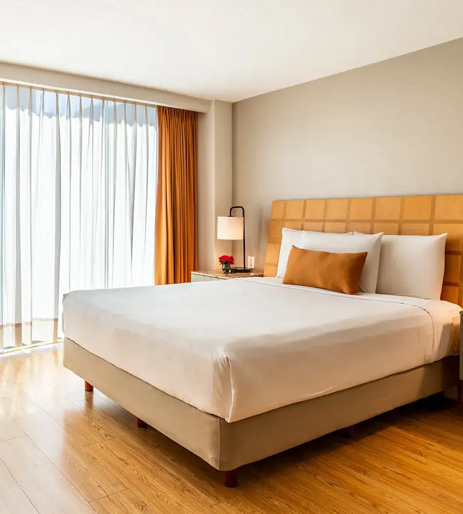 Habitaci&oacute;n de hotel con cama matrimonial, cortinas y l&aacute;mpara junto a ventana