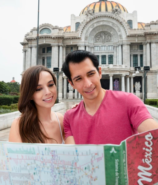 Pareja sonriente frente a un edificio hist&oacute;rico, mostrando un mapa.