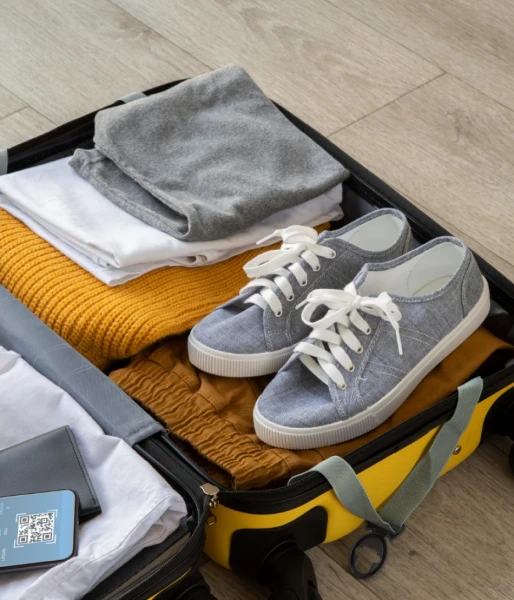 Bolso con ropa doblada y zapatillas grises sobre piso de madera