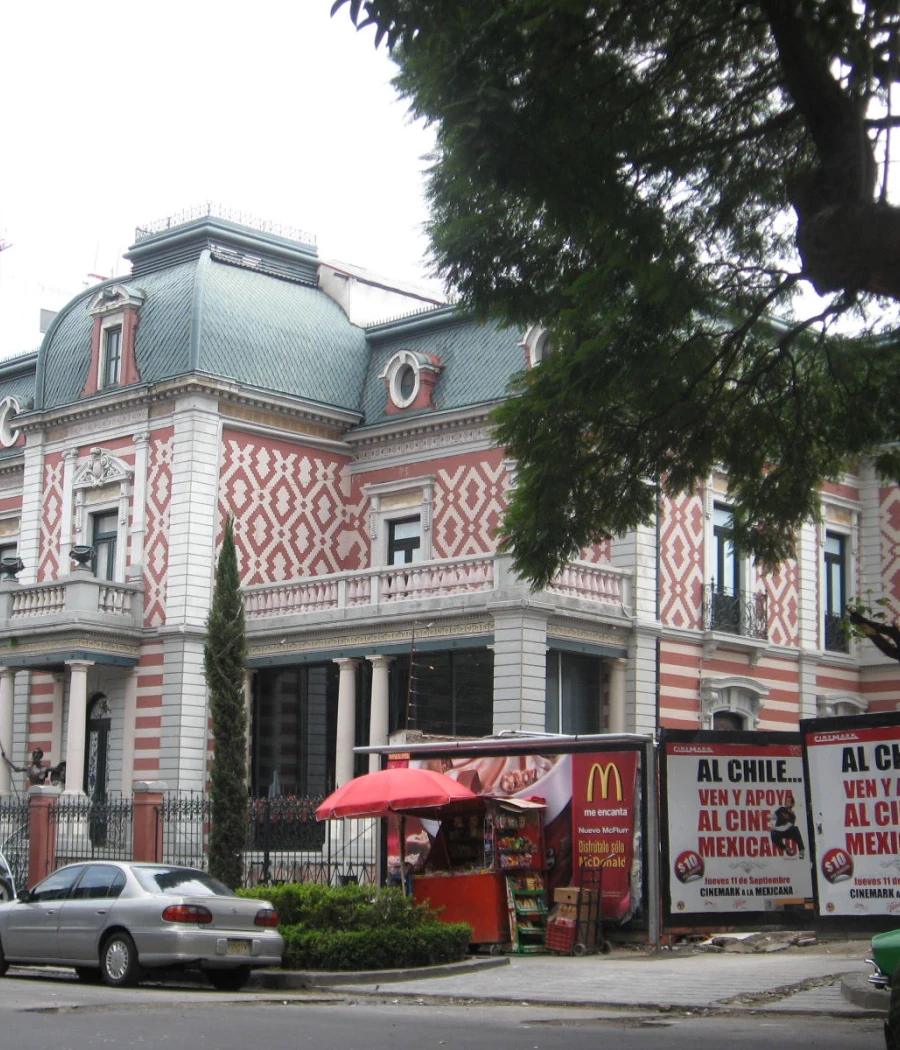Fachada de edificio con cúpula verde y puesto de comida con toldo rojo en la calle