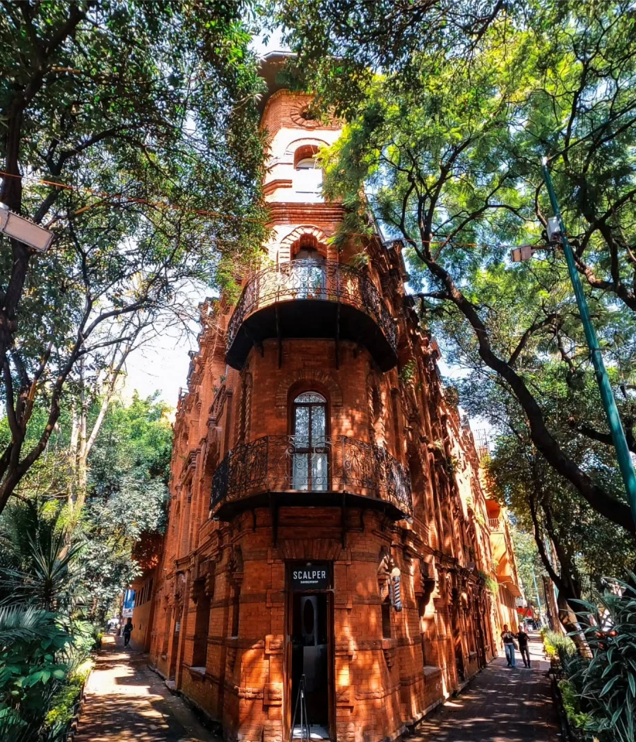 Torre de ladrillo colonial con arcos y balcones entre árboles verdes.