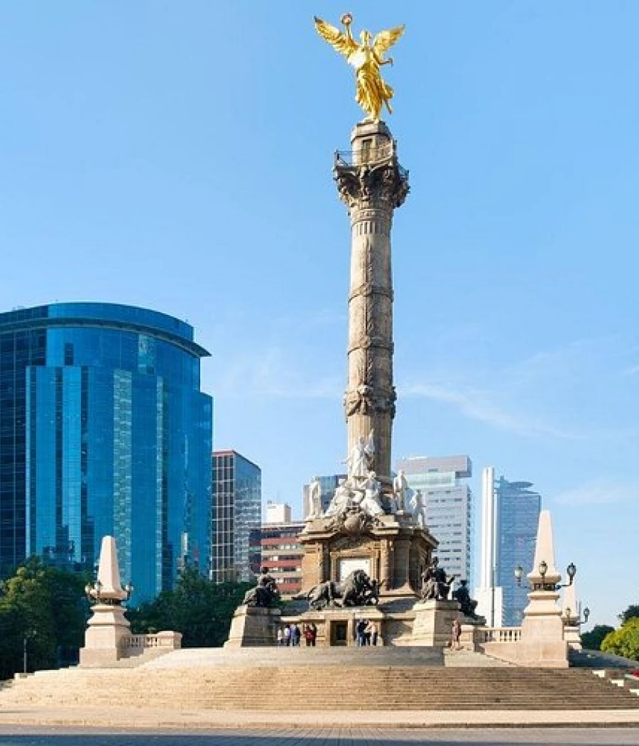 Monumento con estatua dorada sobre columna, en plaza frente a edificios