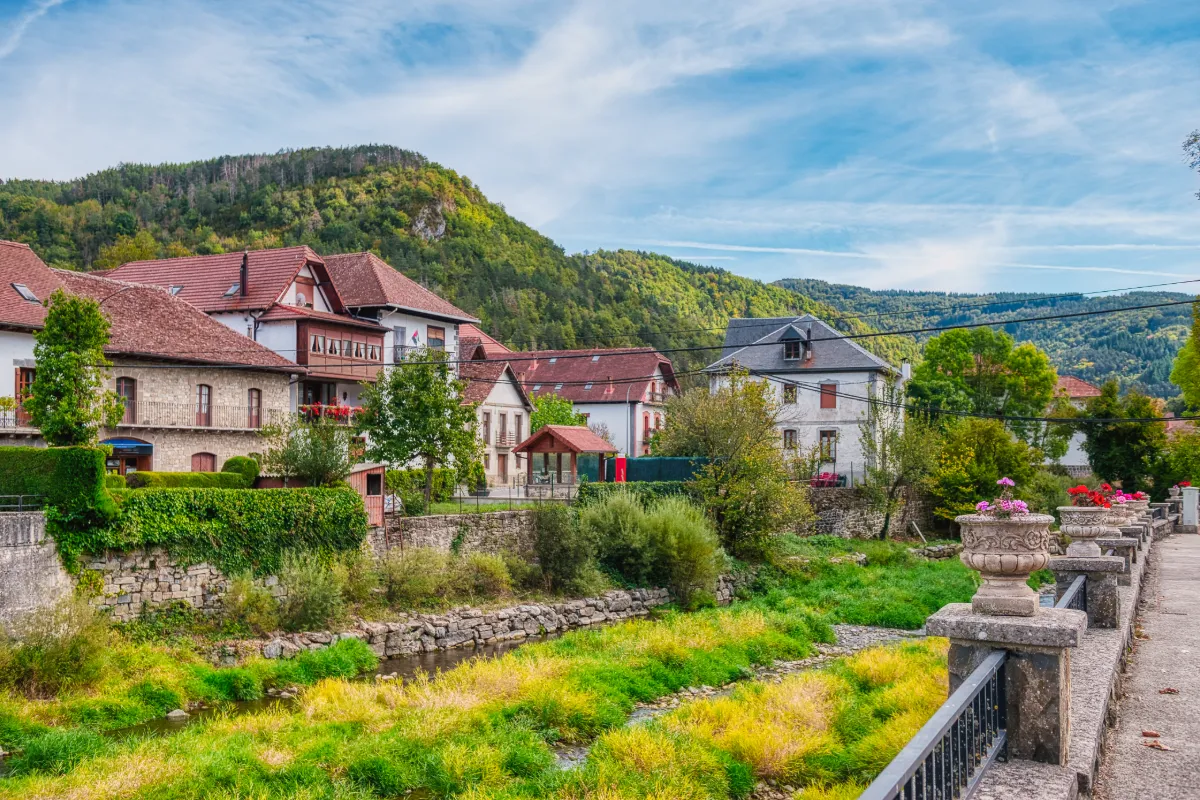 Casas antiguas con jard&iacute;n verde y fuente, en un paisaje monta&ntilde;oso con cielo azul