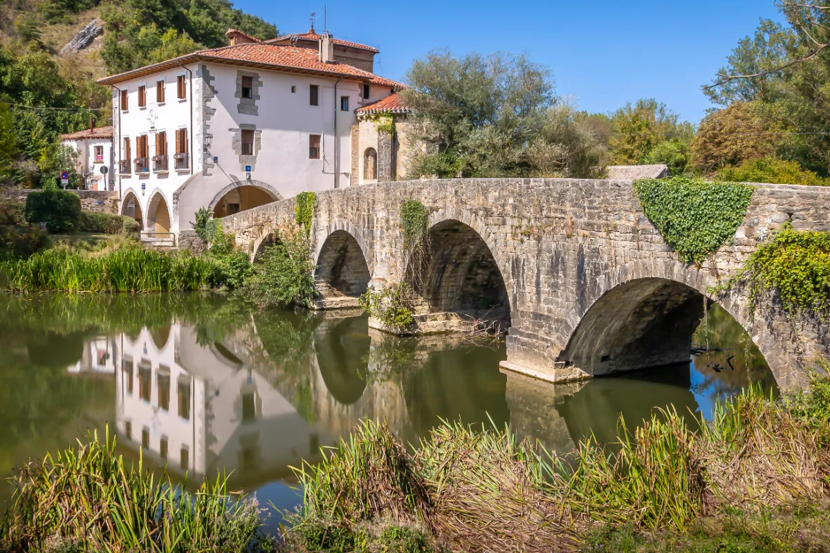 Puente de piedra y casa blanca reflejados en un estanque junto a un r&iacute;o