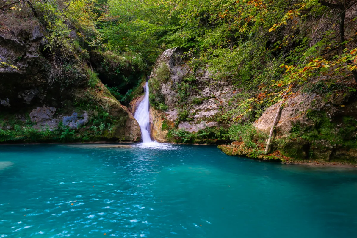 Cascada cae en un ca&ntilde;&oacute;n con agua turquesa y vegetaci&oacute;n verde oto&ntilde;al