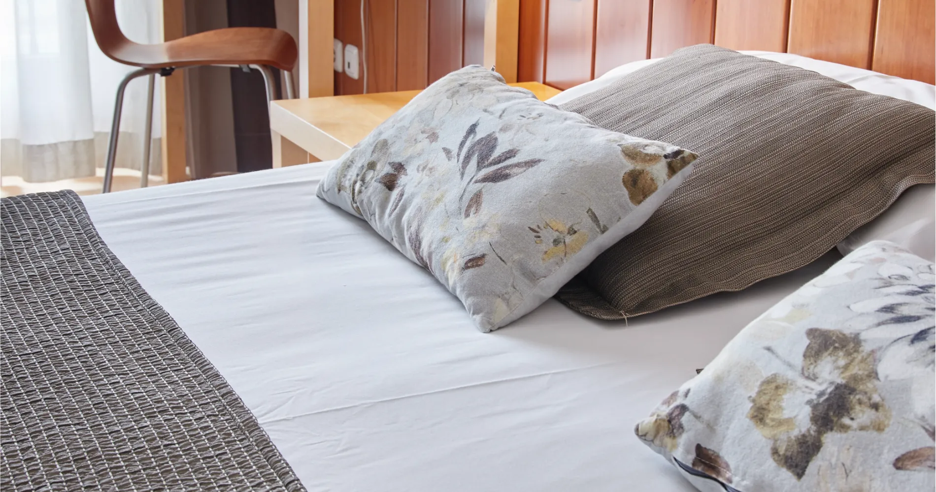 Cama con cojines estampados en habitaci&oacute;n con muebles de madera