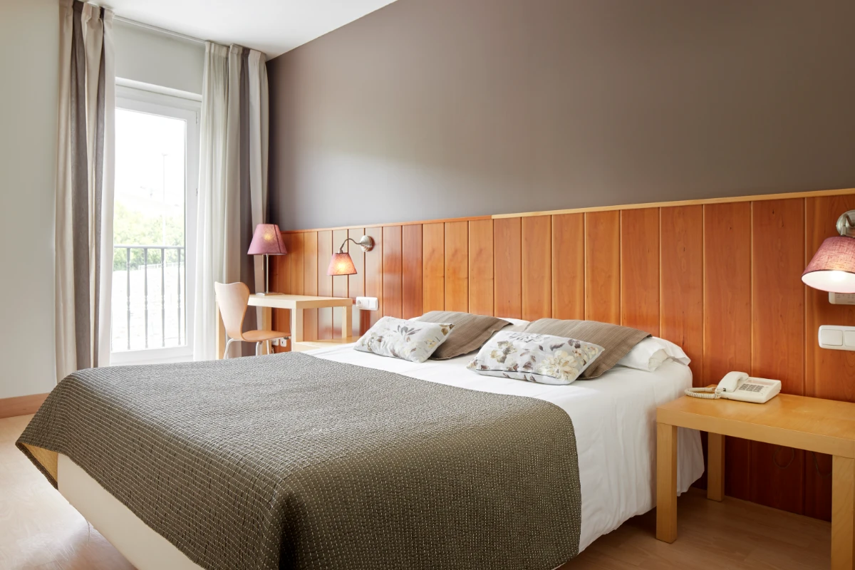 Dormitorio con cama doble, cabecero de madera, cortinas y l&aacute;mparas de mesa