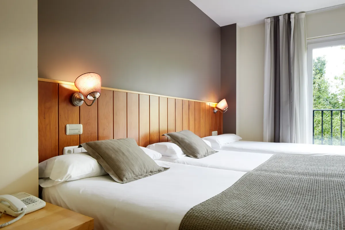 Dormitorio moderno con cama doble, l&aacute;mparas y ventana con cortinas.