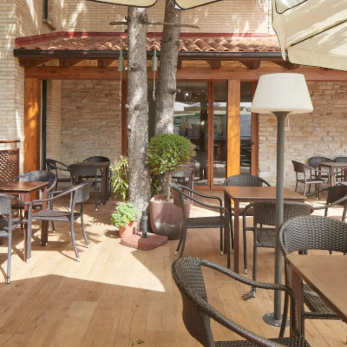 Patio con sillas y mesas de terraza, sombrilla y pilares de piedra al sol
