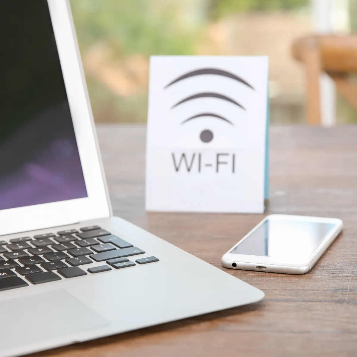 Laptop con pantalla blanca, smartphone y tarjeta &ldquo;WI-FI&rdquo; en escritorio