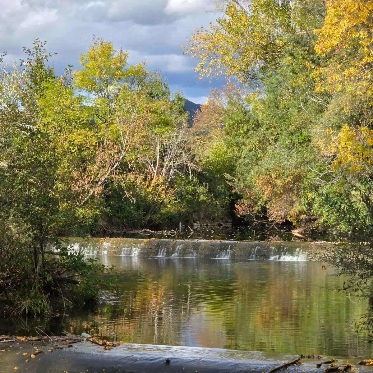R&iacute;o con cascada, &aacute;rboles oto&ntilde;ales y reflejo en agua tranquila