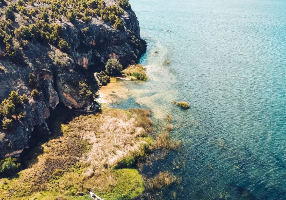 Acantilados verdes y playa rocosa junto al mar turquesa con lanchas ancladas