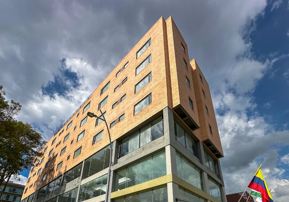 Edificio moderno de ladrillo con banderas y ventanales, bajo cielo nublado