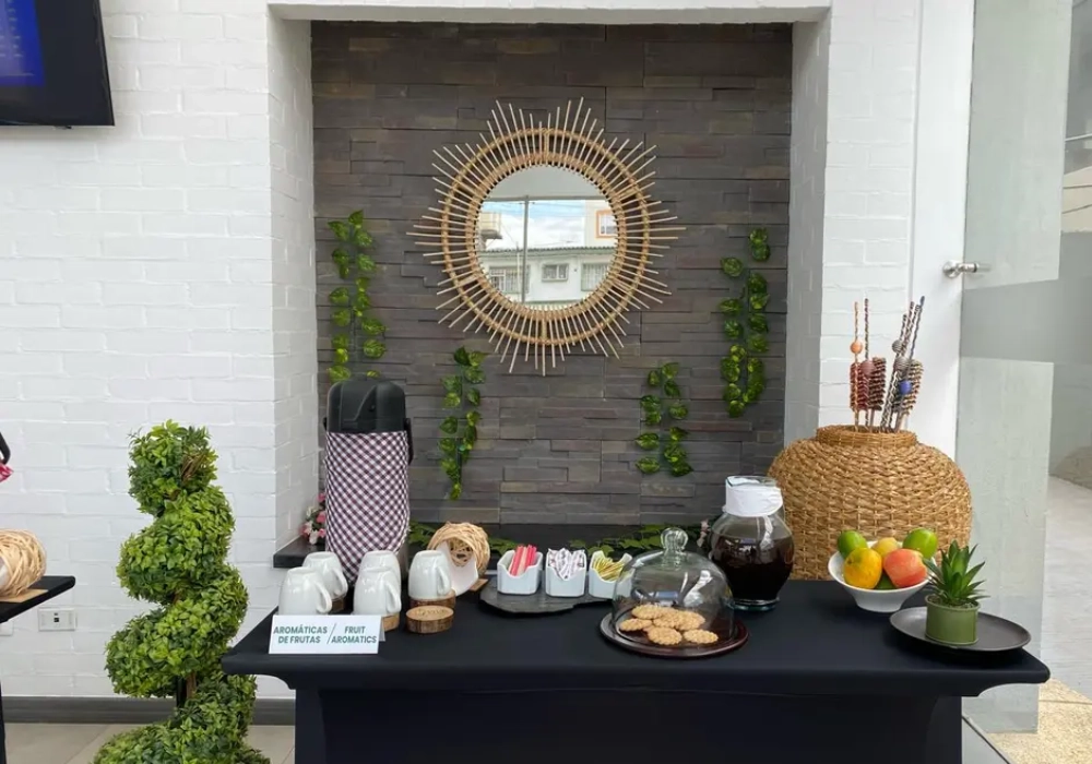 Mesa de buffet con bebidas y decoraci&oacute;n verde, junto a un espejo decorativo.