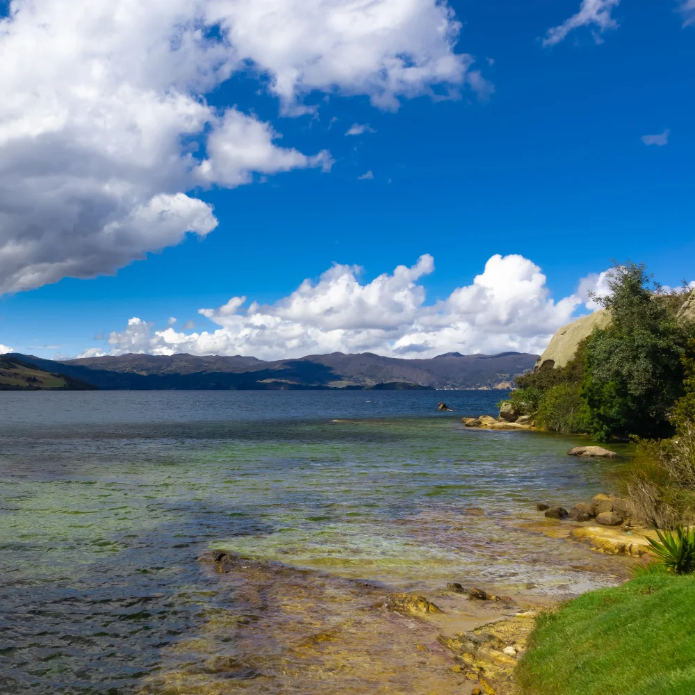 Lago con aguas verdes, costa y monta&ntilde;as bajo cielo azul con nubes.