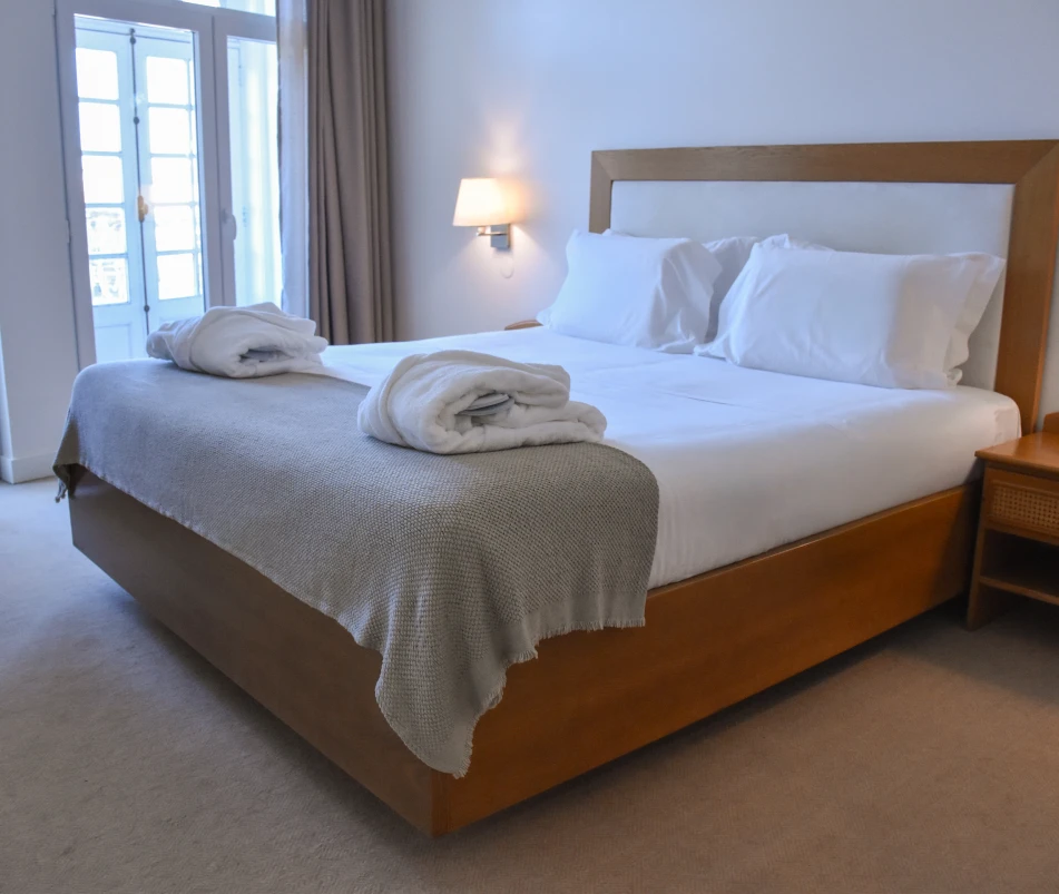 Quarto de hotel com cama de madeira, lençóis brancos e cobertor cinza