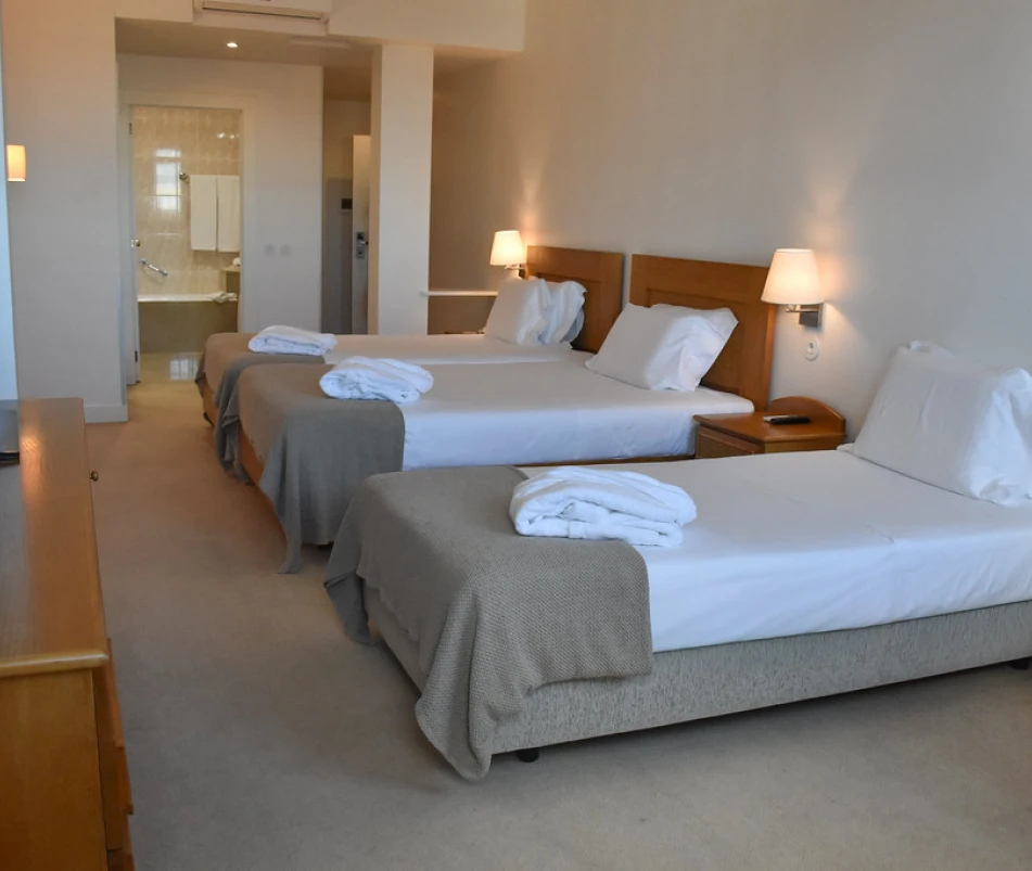 Quarto de hotel com duas camas, luminárias e roupas dobradas sobre elas