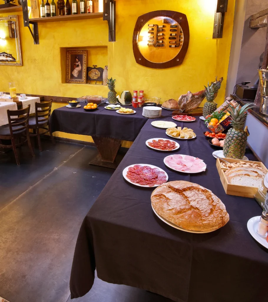 Mesa de buf&eacute; con embutidos, panes, pi&ntilde;as y bebidas en un comedor r&uacute;stico