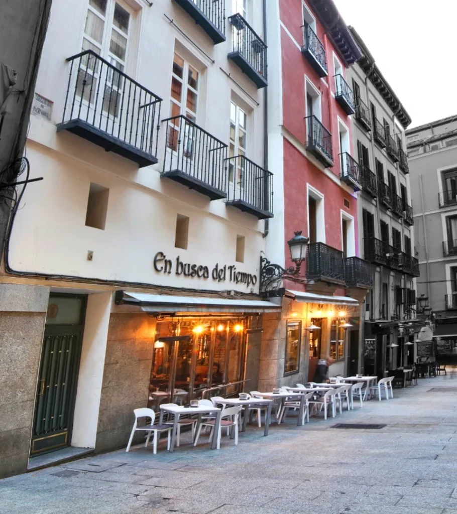 Calle estrecha con balcones y mesas blancas junto a un restaurante iluminado