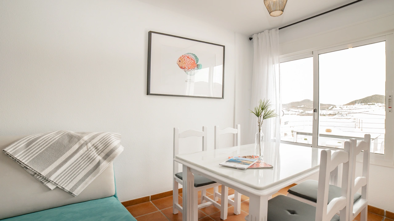 Comedor luminoso con mesa blanca, sillas y cortinas junto a la ventana