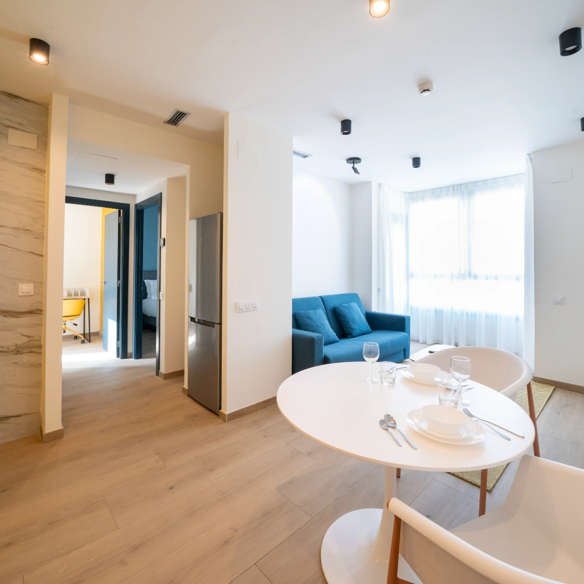 Sala de estar moderna con mesa redonda, sof&aacute; azul y luz cenital
