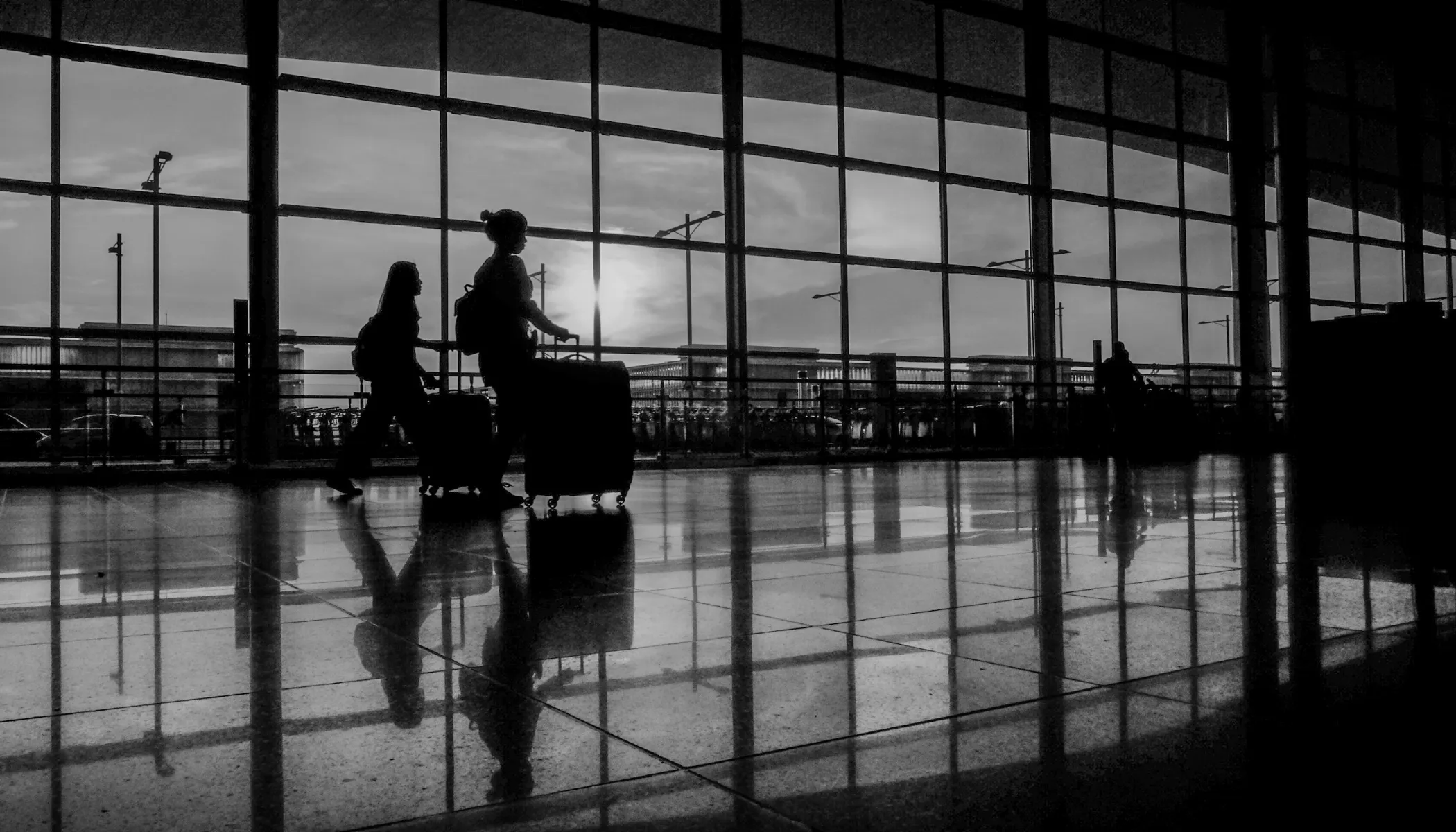 Silhuetas de dos personas con maletas caminando en un andén, en blanco y negro