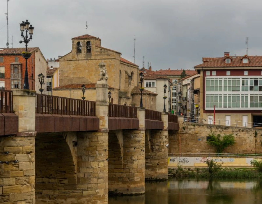 Puente con piedra antigua y edificios al fondo junto a un r&iacute;o.