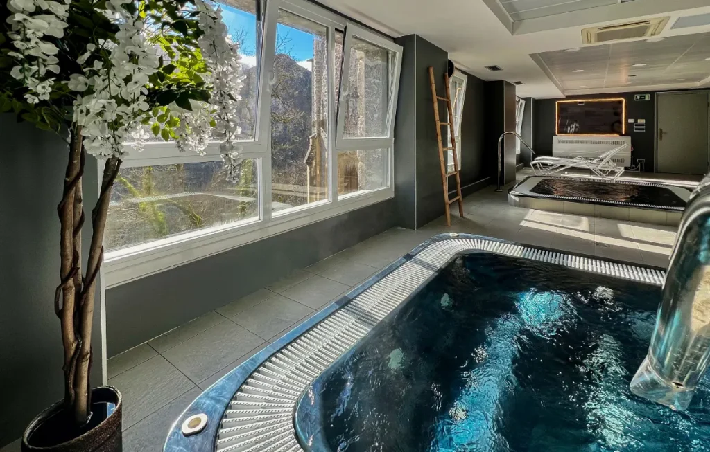 Interior de spa con jacuzzi y ventana, flores blancas y zona de sauna.