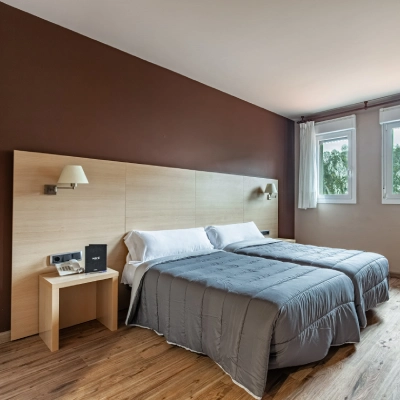 Dormitorio moderno con cama doble, mesita y ventana con cortinas.