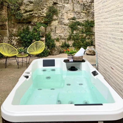 Jacuzzi blanco al aire libre con pared de piedra y cojines.