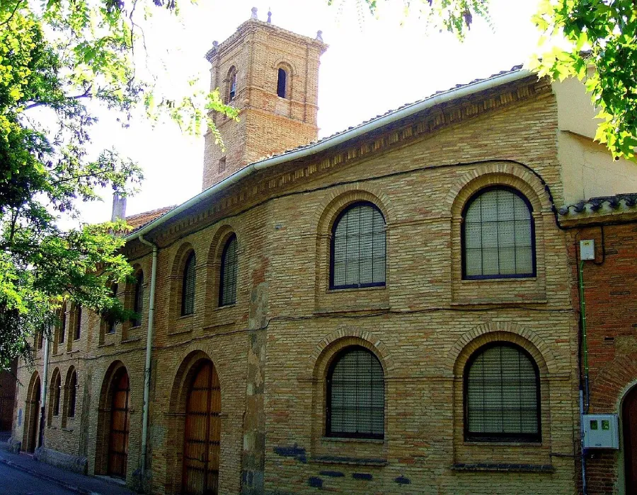 Iglesia de ladrillo con arcos, ventanas y torre campanario, entre &aacute;rboles