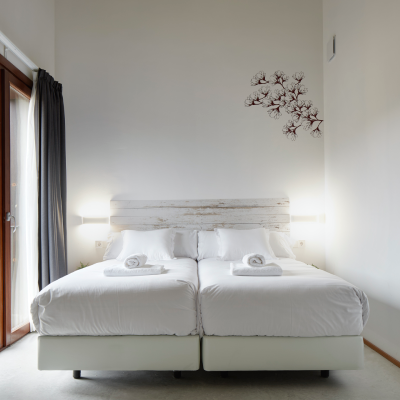 Habitaci&oacute;n con cama doble blanca y l&aacute;mparas de pared, decoraci&oacute;n floral.